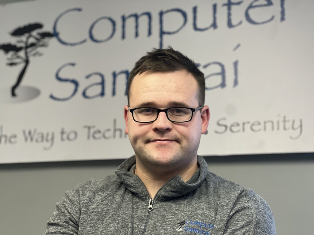 A man in glasses and a jacket standing next to a sign.